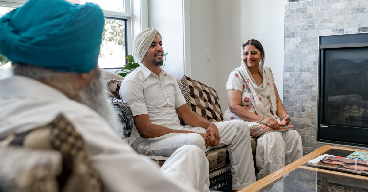 Family members in traditional attire having a conversation on the sofa in a bright living room.
