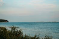 一个宁静的看法海洋与遥远的山丘和郁郁葱葱的前景绿色植物下一个明确的蓝天