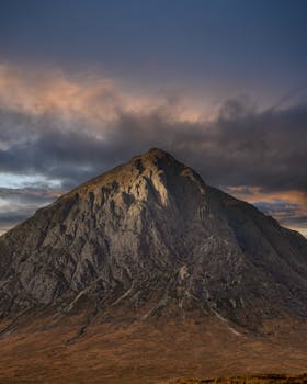A stunning view of a rugged mountain peak under a dramatic moody sky during sunset.