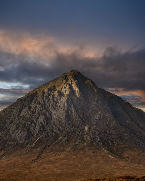Free A stunning view of a rugged mountain peak under a dramatic moody sky during sunset. Stock Photo
