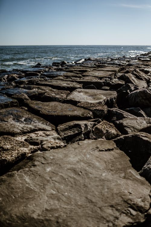 Free A scenic view of a rocky coastline with the ocean stretching into the horizon under a clear blue sky. Stock Photo