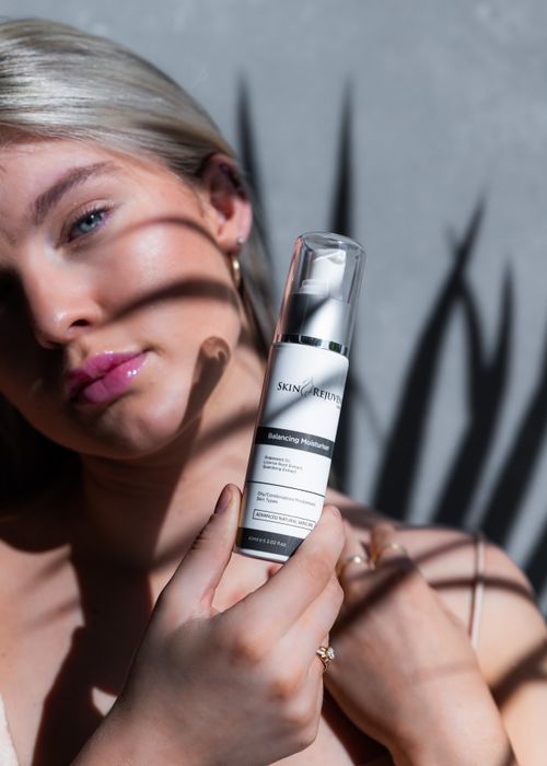 Free Close-up of a young woman displaying a skincare serum in bright sunlight with artistic shadows. Stock Photo
