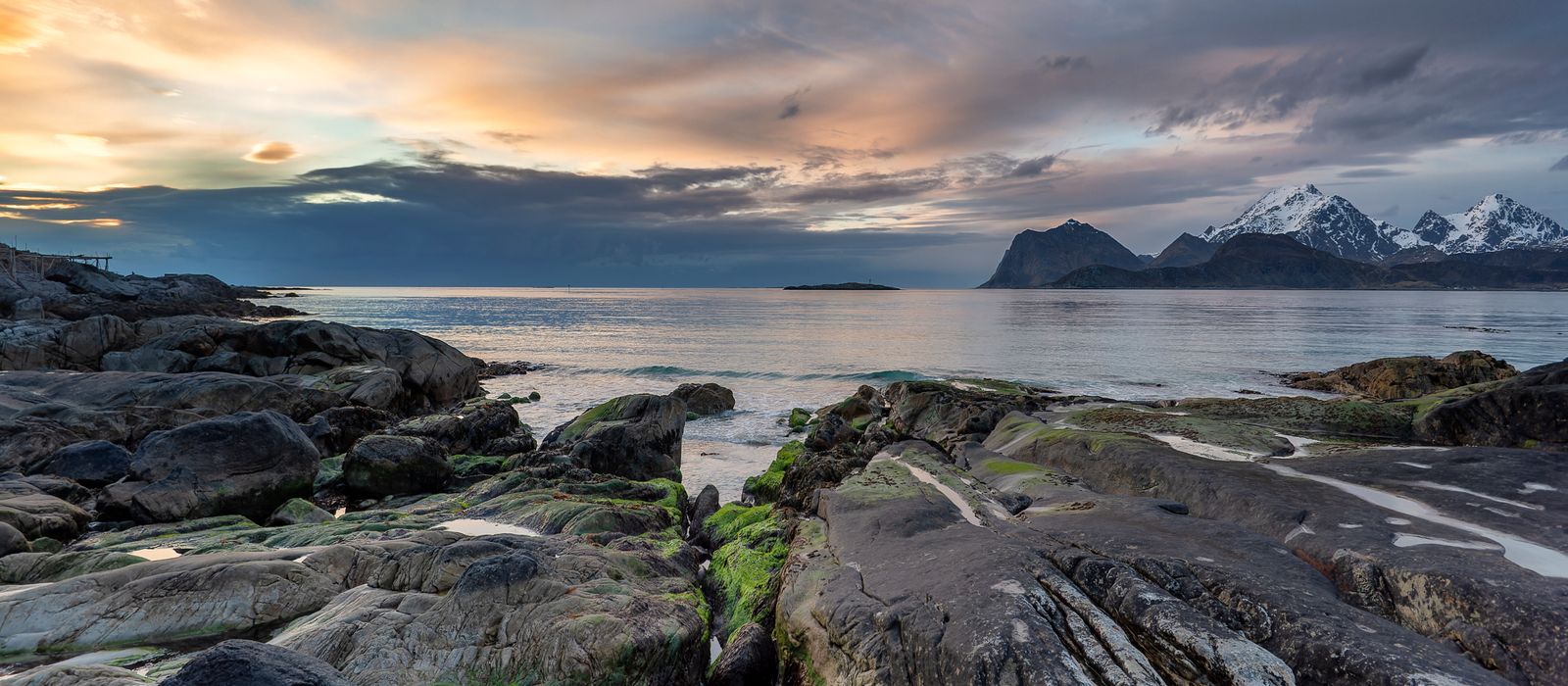 Low night sun over a rocky Norwegian coastline with mountains along the horizon.
