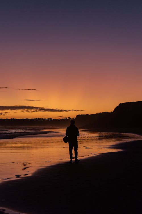Silhouette of a Person on the Shore During Sunset