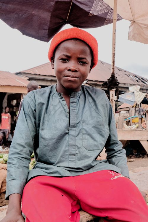 Free A young boy wearing a hat and casual clothing at an outdoor market, smiling at the camera. Stock Photo