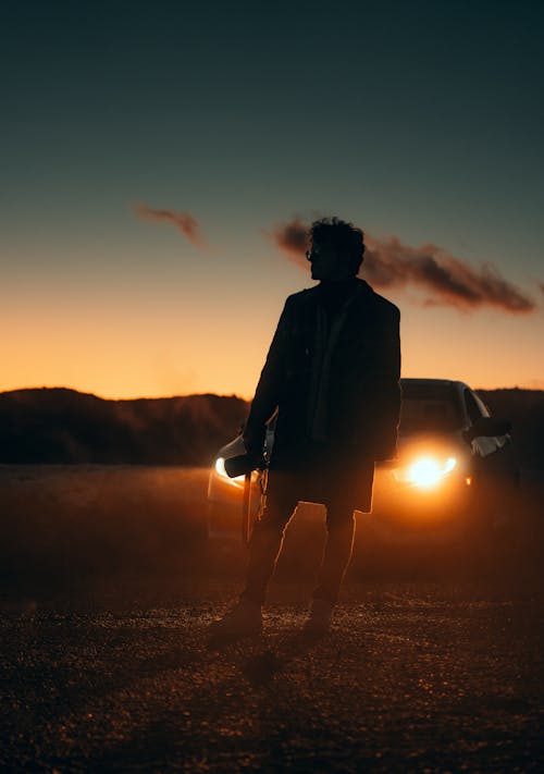 A Silhouette Photographer in front of a Car with the Headlights On