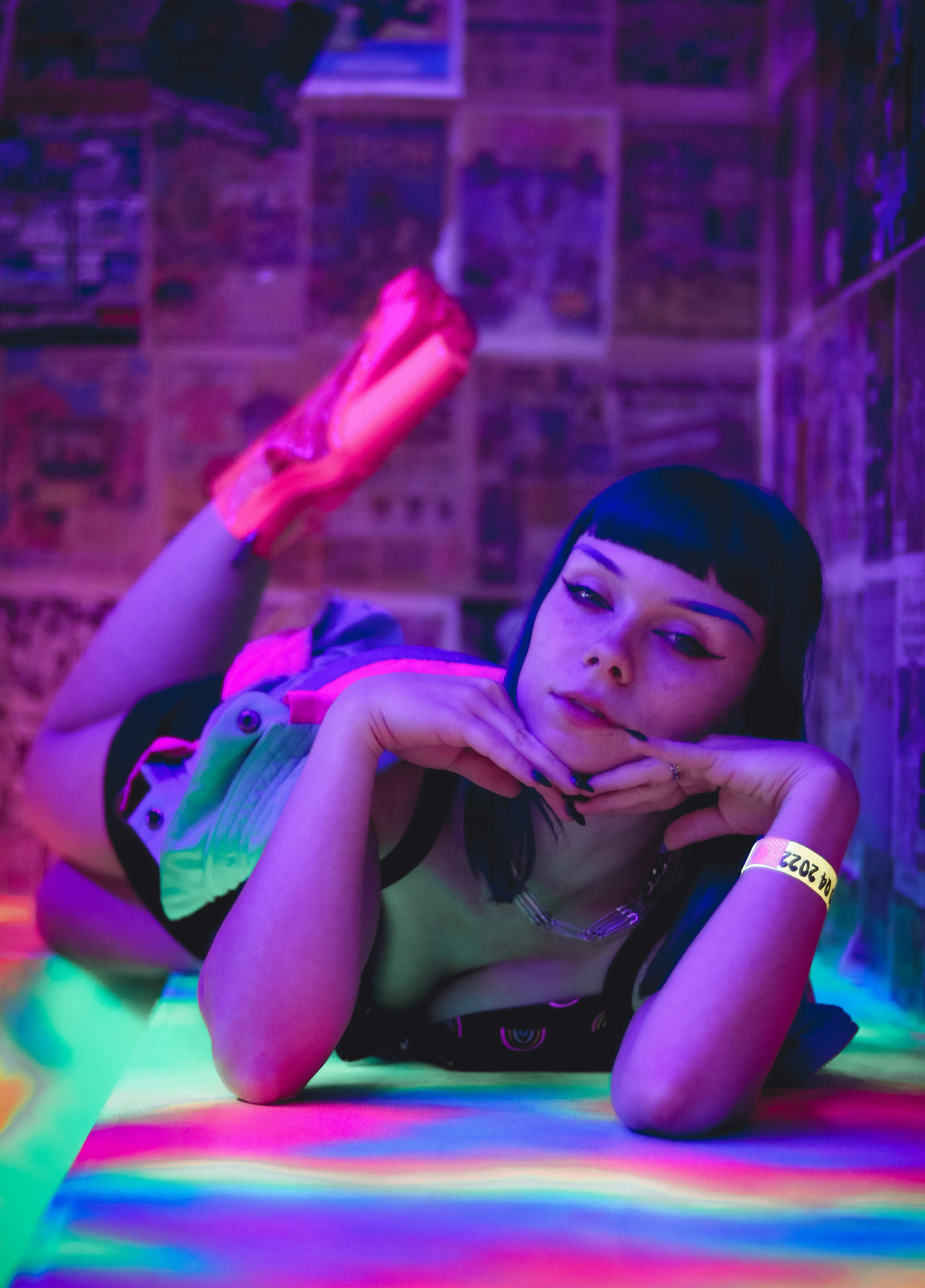 A woman posing with hands on chin in a vibrant, neon-lit room.