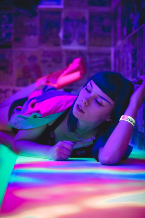 Free A woman poses creatively under ultraviolet purple lighting in a vibrant nightclub setting. Stock Photo