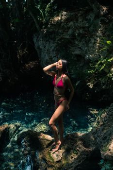 A woman in a red bikini poses by a serene rock pool surrounded by lush greenery.