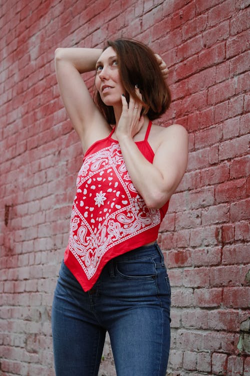 A Woman in Red Tank Top Standing on the Street Near the Brick Wall