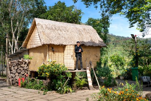 Free A man standing by a bamboo cottage surrounded by lush plants, showcasing rural living. Stock Photo