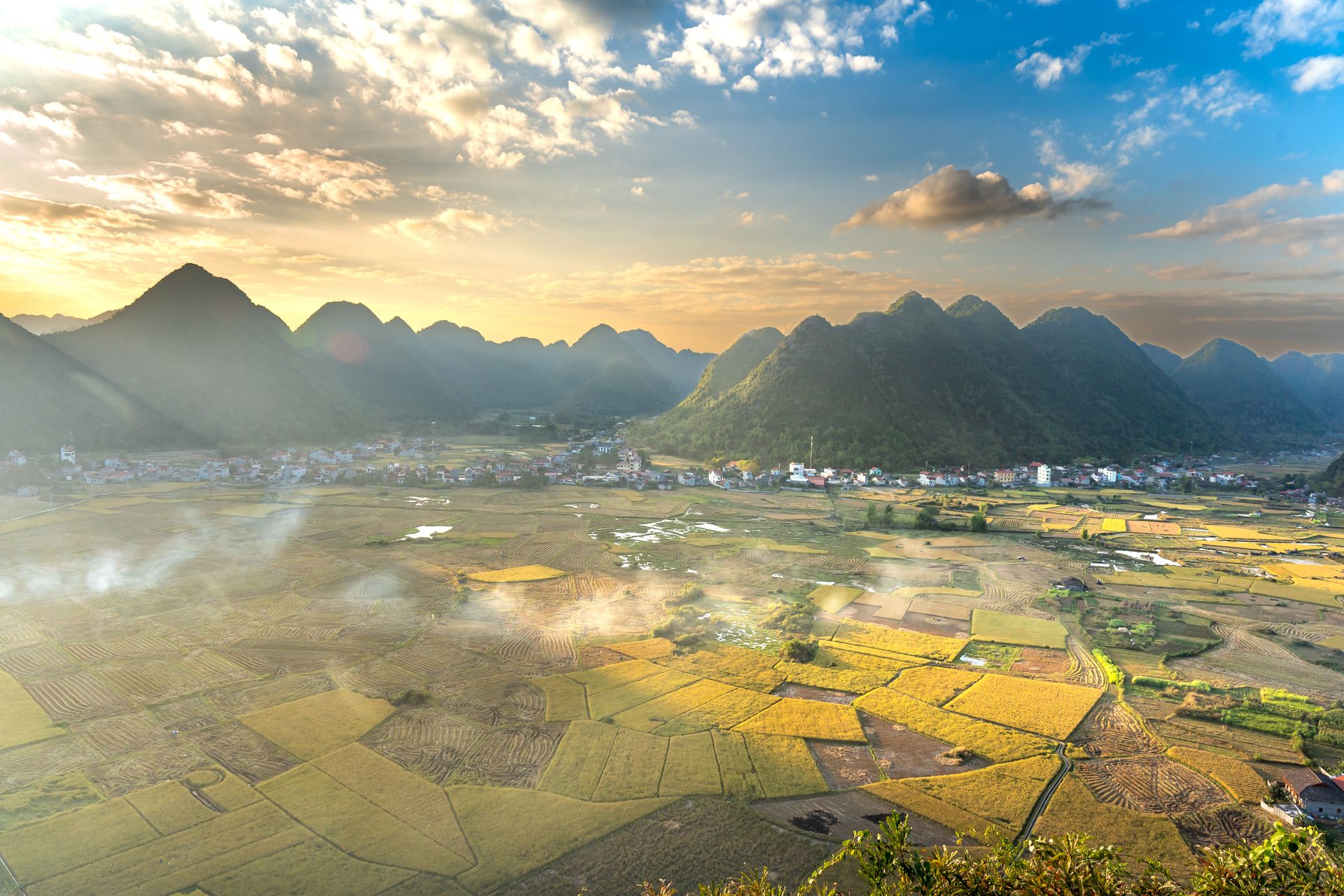 Breathtaking aerial view of vast agricultural fields and mountains bathed in sunrise light.