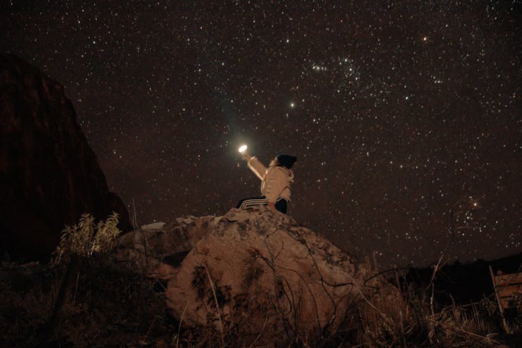 Woman With Light Sitting On Hill Against Starry Sky