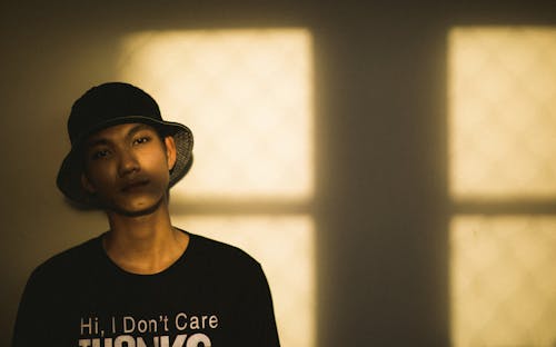 A Man in a Black Shirt and a Bucket Hat Leaning on a Concrete Wall