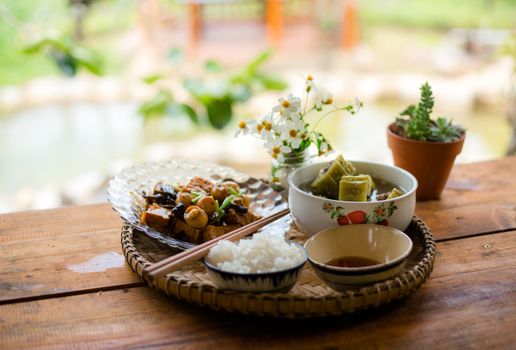 A vibrant Asian meal with rice, vegetables, and decorative flowers on a wooden table.