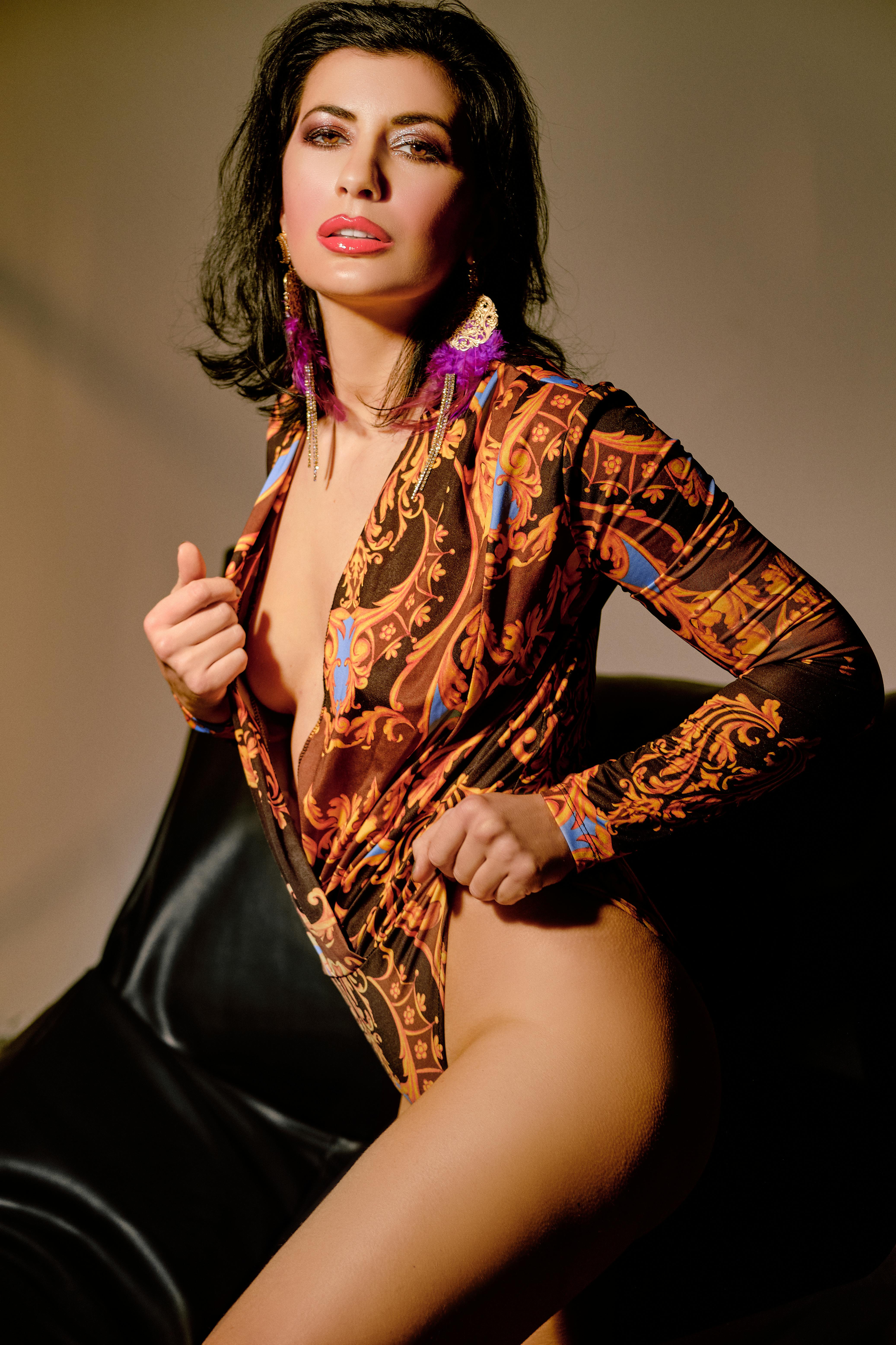 Confident woman in ornate printed shirt posing indoors with stylish accessories.