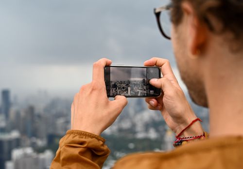 Free Man photographing Bangkok's skyline with smartphone on a cloudy day. Stock Photo