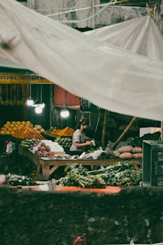 An Indonesian market stall with a woman selling a variety of fresh fruits and vegetables.
