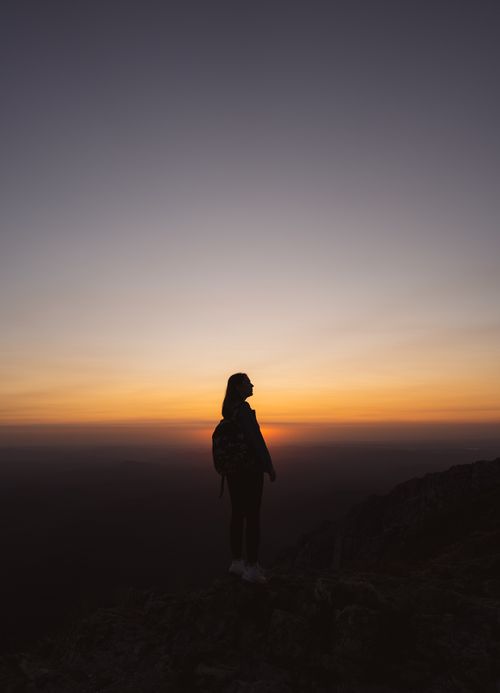 Free A woman stands silhouetted against a vibrant sunset on a mountain peak. Stock Photo