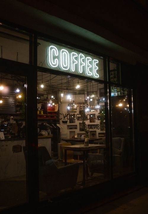 Free A charming view of a café interior at night, featuring a glowing neon coffee sign. Stock Photo