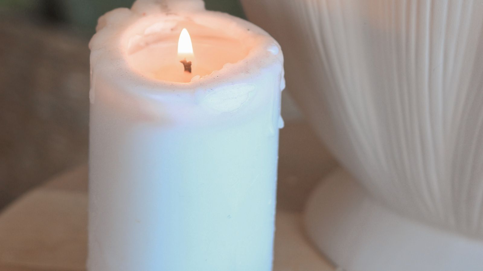 A lighted white candle beside a vase of small white flowers