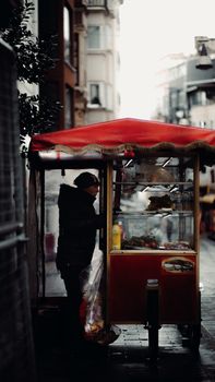 A street vendor in Istanbul serves food from a cart on a rainy day, capturing urban life.