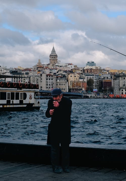 Man in Black Coat Smoking Cigarette Near Body of Water 