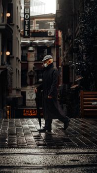 A man in a hat and mask walks on a rainy Istanbul street, reflecting a moody urban vibe.