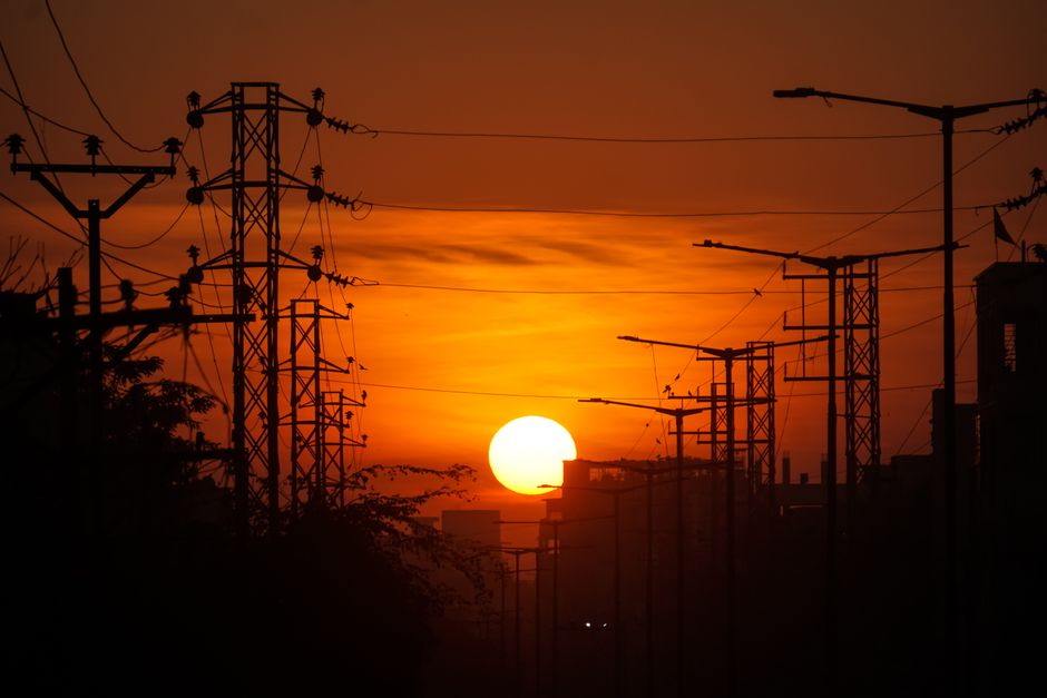 Power lines in silhouette against an orange sunrise sky, symbolizing energy and industry.