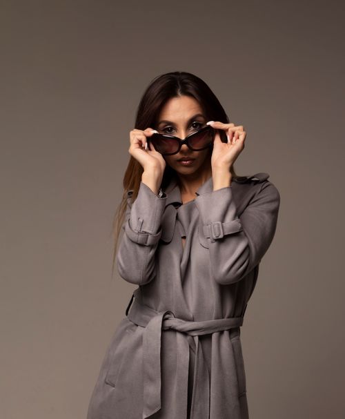 Free Fashionable woman in sunglasses and trench coat posing in a studio setting. Stock Photo