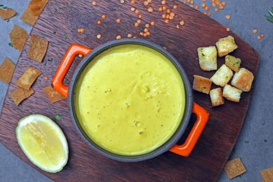 Smooth yellow red lentil soup in orange-handled pot with croutons, lemon half and lentils