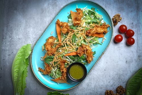 Free Delicious crispy chicken salad on a blue plate with fresh greens and walnuts. Stock Photo
