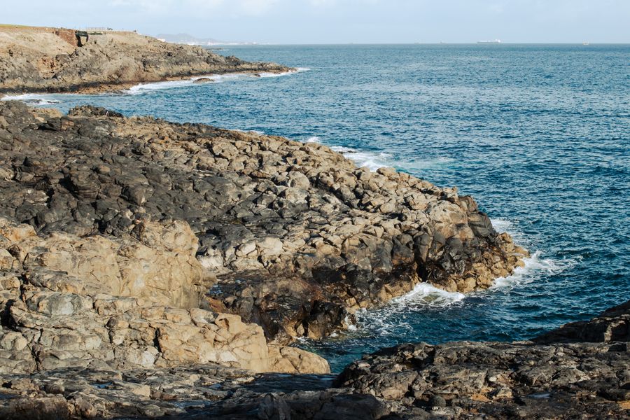 Explore the rugged rocky shoreline meeting the blue sea, capturing nature's raw beauty.