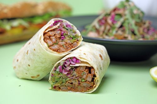 Free Tasty chicken wrap with fresh vegetables and a side salad on a light green background. Stock Photo
