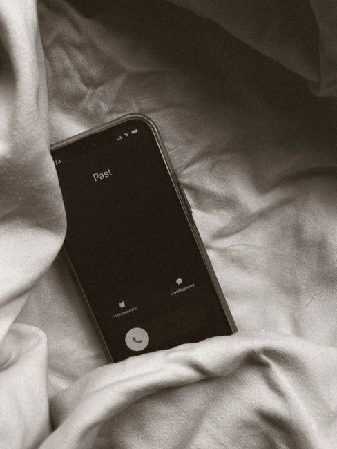 A smartphone on a bed displays an incoming call from 'Past' in a cozy, indoor setting.