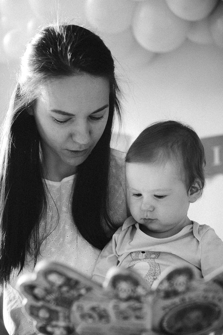 Grayscale Photo Of A Woman Reading Book With A Baby