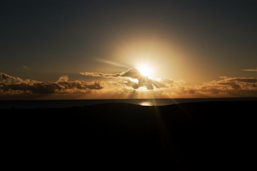 Free Sunlight over Silhouette of Hill on Sea Coast at Sunset Stock Photo