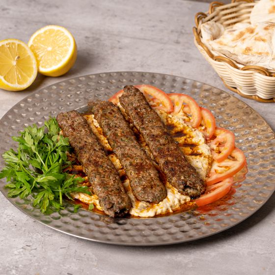 Three long minced meat kebabs on garlic yogurt with chili butter, tomato slices, parsley and lemon