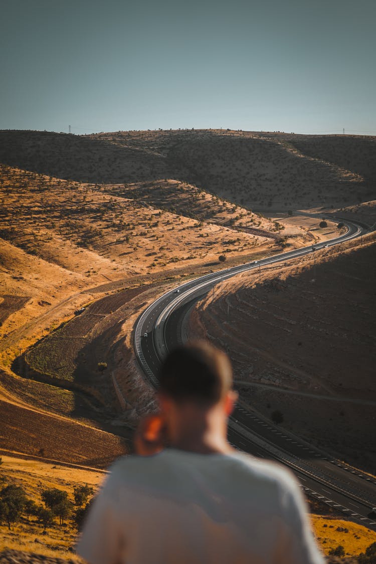 Back View Of A Man Standing On The Hill With The View On A Desert And Road 