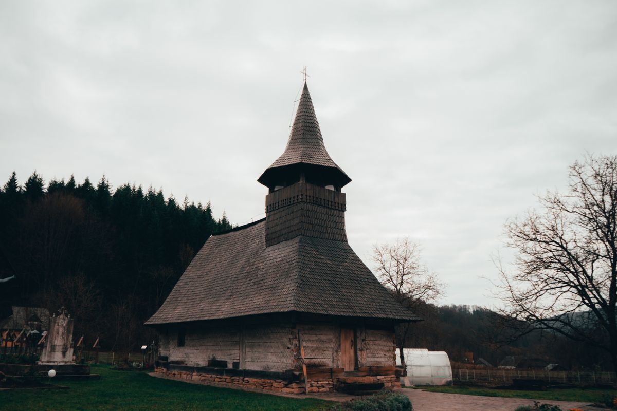 Biserica de lemn cu sindrila si turla inalta, langa padure