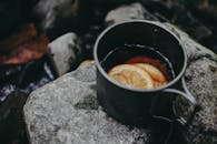 溪流旁的岩石上，放着一个装有热饮和柠檬片的金属杯，营造出迷人的户外场景