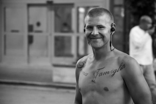 A shirtless man with tattoos and a headset smiling outside.