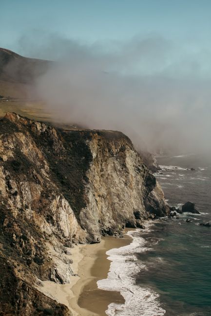 A stunning aerial view of rugged cliffs meeting the sea under a misty sky.