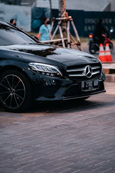 Black Mercedes-Benz C Class parked in an urban area with traffic cones and pedestrians in view.
