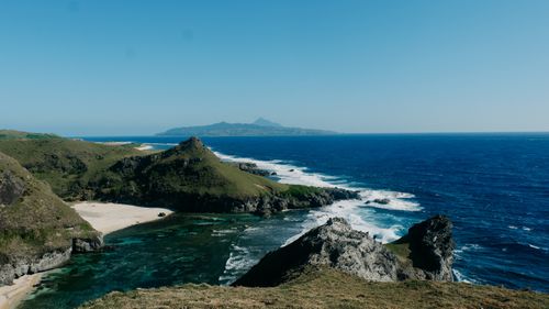 Free Breathtaking coastal scenery depicting rugged cliffs, clear blue sea, and distant mountains. Stock Photo