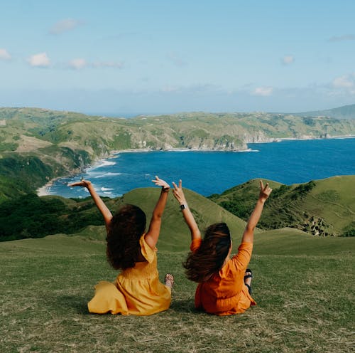 Young Women in Orange Dresses Sitting on a Hill near the Shore 