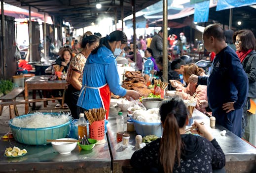 Bustling street food market scene with vendors and customers enjoying diverse Asian cuisine.