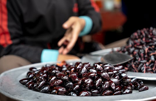 Close-up of fresh dark berries on a vendor's plate at a bustling street market.