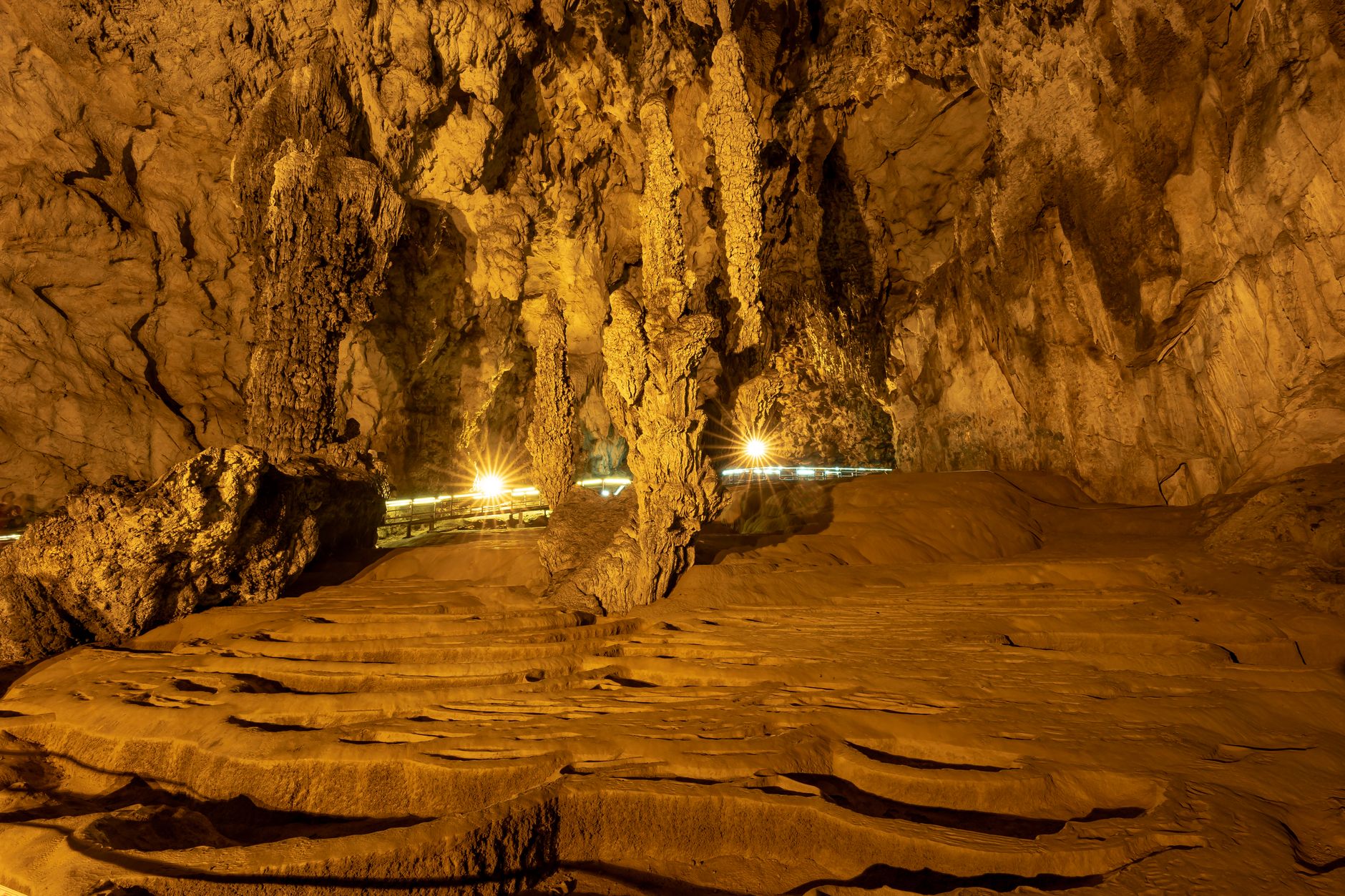 Explore the mesmerizing formations of a grand cave with illuminated stalactites and stalagmites.