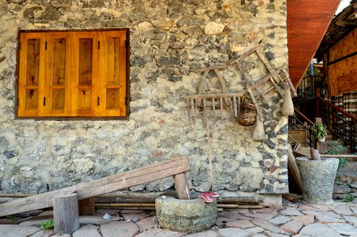 Free A rustic stone wall featuring wooden shutters and antique tools adds vintage charm. Stock Photo